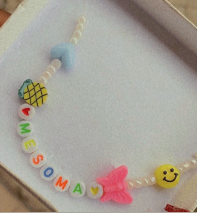 Handmade bracelet with various beads spelling out ‘MESOMA’ on a white surface